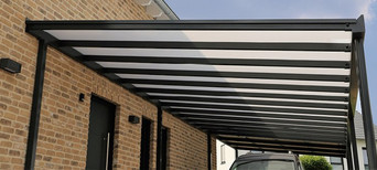 Moderne Überdachung mit transparenter Dacheindeckung aus Kunststoffplatten und stabiler Metallkonstruktion.