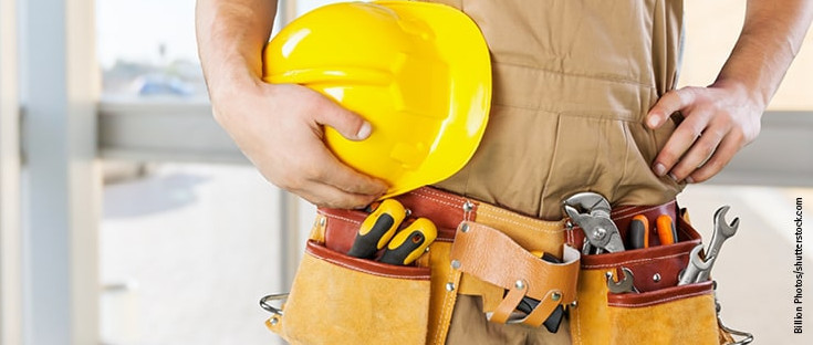 Handwerker mit gelbem Schutzhelm und Werkzeuggürtel, bereit für den Einsatz auf der Baustelle.