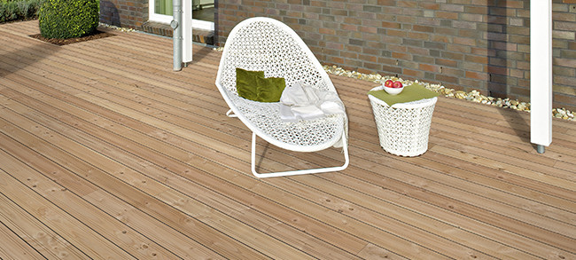 Helle Holzterrasse neben einem Gebäude mit Terrassensessel und dekorativen Elementen.