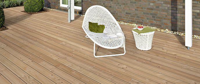 Helle Holzterrasse neben einem Gebäude mit Terrassensessel und dekorativen Elementen.
