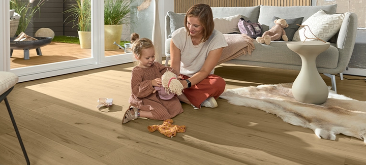 Helles Parkett im Wohnzimmer. Eine Frau spielt mit einem kleinen Mädchen auf dem Boden.