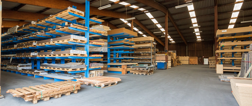 Große Lagerhalle mit blauen Regalen voller Holzplatten und Paletten auf dem Boden.