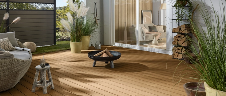 Helle Terrasse vor einem Haus, umgeben von einem Sichtschutzzaun mit dekorativen Elementen.