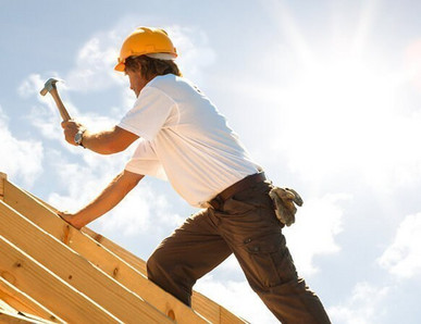 Dachdecker mit gelbem Schutzhelm beim Befestigen von Konstruktionsvollholz (KVH) auf einem Dachstuhl unter strahlendem Himmel.
