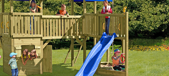 Kinderspielplatz mit Turm, Brücke und Rutsche. Kinder rutschen, klettern und spielen auf der Wiese.
