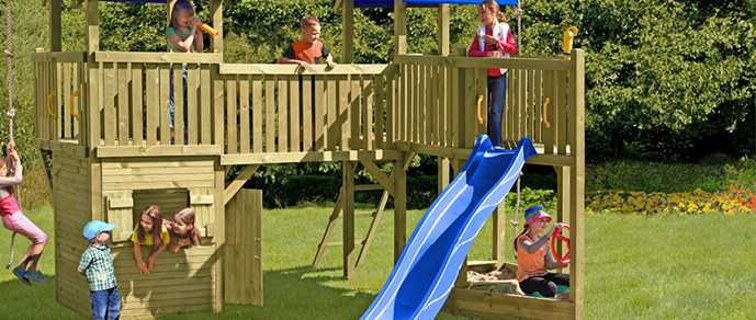 Kinderspielplatz mit Turm, Brücke und Rutsche. Kinder rutschen, klettern und spielen auf der Wiese.