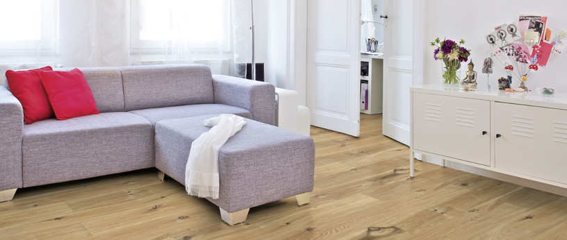 Im Wohnzimmer ist Parkett in Langdielen-Optik verlegt. Dazu passt ein Ecksofa mit bunten Kissen.
