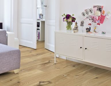 Im Wohnzimmer ist Parkett in Langdielen-Optik verlegt. Dazu passt ein Ecksofa mit bunten Kissen.